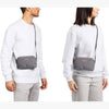 Two people wearing white sweaters with gray crossbody bags on a white background