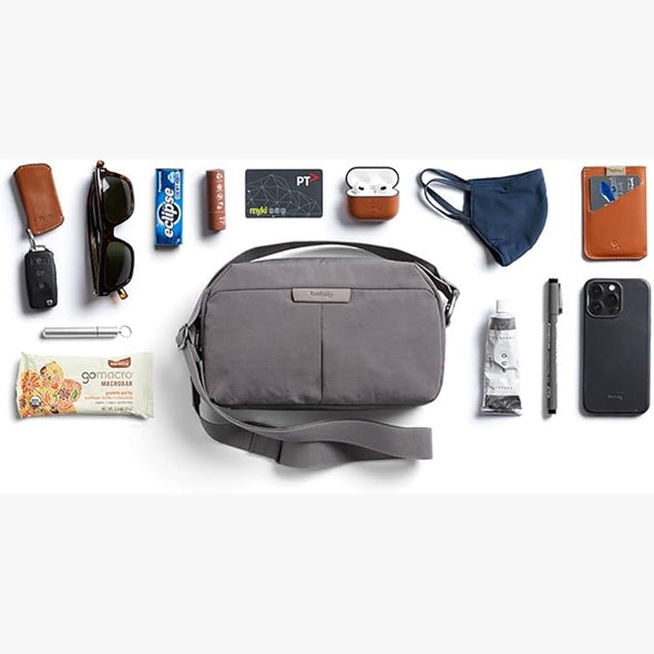 Gray shoulder bag with various items arranged around it on a white background
