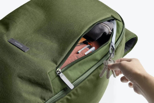 Green backpack with a hand reaching in to open it, revealing keys and a phone.