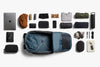 Collection of travel items arranged around an open blue backpack on a white background