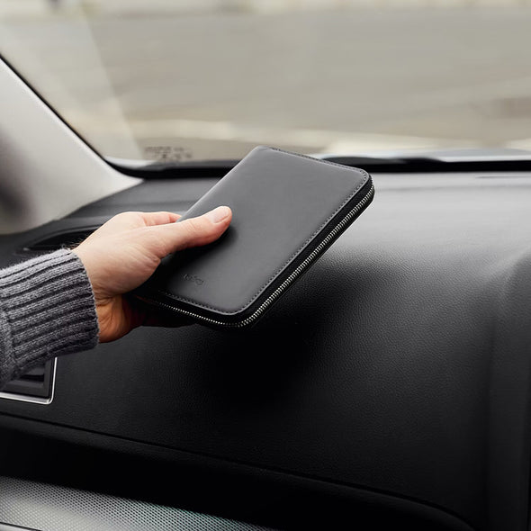 Person holding a black zippered pouch on a car dashboard