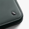Close-up of a dark green leather wallet with a brand logo on a light gray background