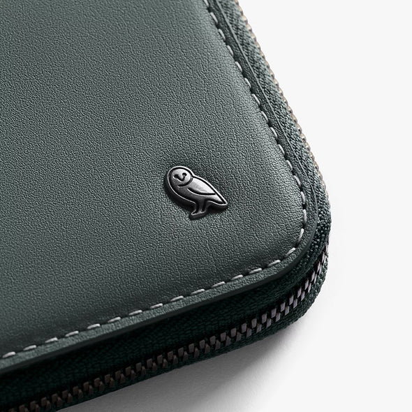 Close-up of a dark green leather wallet with a brand logo on a light gray background