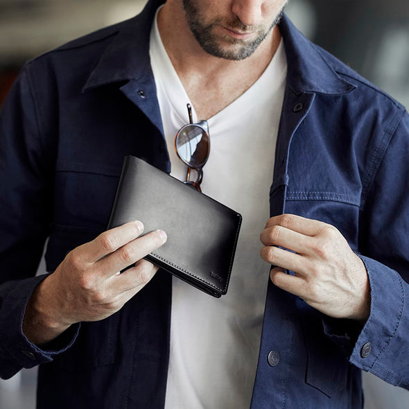 Man holding a black wallet with sunglasses on a blurred background