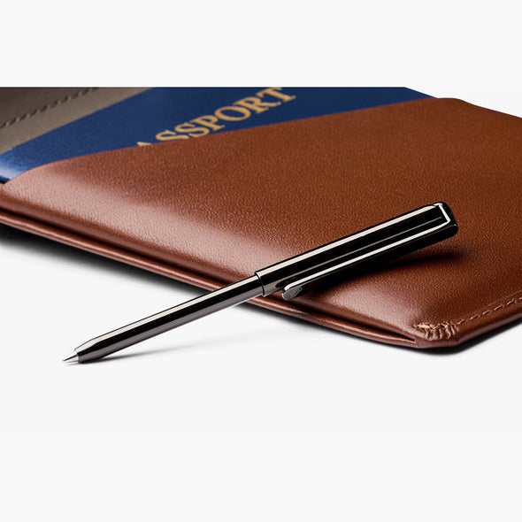 Pen on a brown leather wallet with a passport in the background