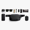 Black waist bag with various items on a white background