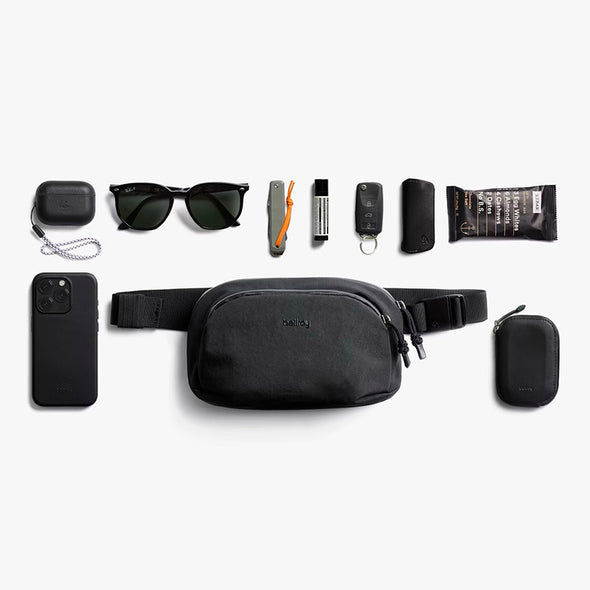 Black waist bag with various items on a white background