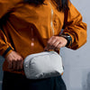 Person holding a gray bag with a brand logo against a neutral background