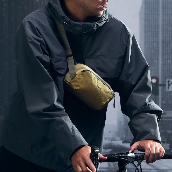 Person wearing a dark raincoat with a yellow bag, standing on a city street.