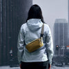 Person wearing a light gray jacket with a yellow bag in an urban snowy setting