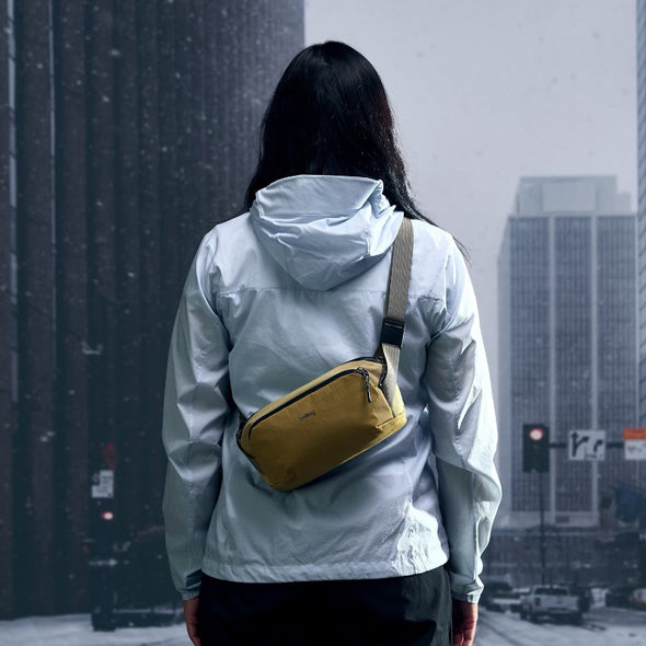 Person wearing a light gray jacket with a yellow bag in an urban snowy setting