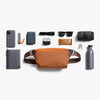 Brown waist bag with various items on a white background