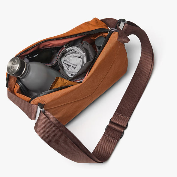 Brown sling bag with items inside on a white background