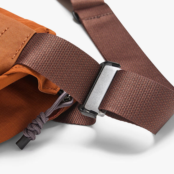 Close-up of a brown strap with a metal buckle on an orange bag.