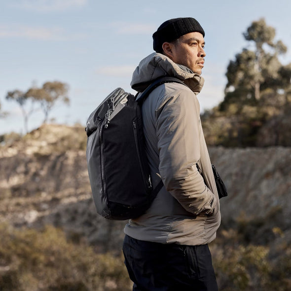 Man with a black backpack standing outdoors with a natural landscape in the background