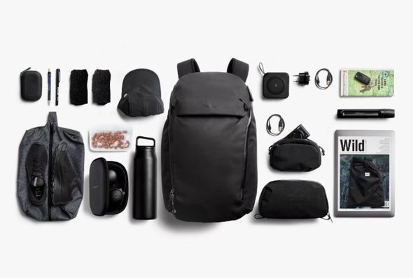 Black backpack with various travel accessories on a white background