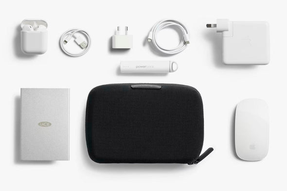 Collection of electronic accessories including a Tech Kit Compact by Bellroy, white mouse, and various cables on a white background.