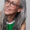 Woman with grey hair and IZIPIZI Reading Glasses Collection #C Blue Tortoise wearing a green top against a plain background