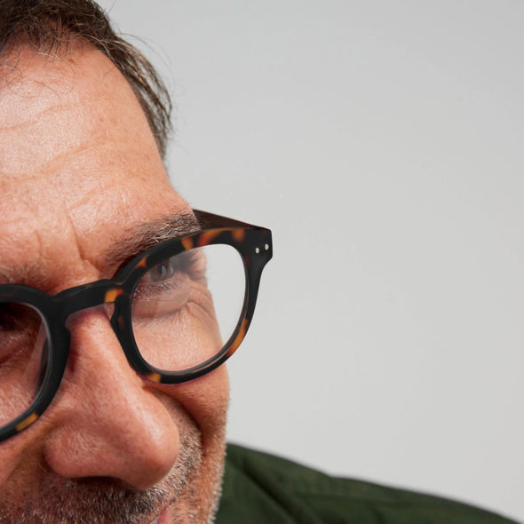 Close-up of a person wearing tortoiseshell glasses IZIPIZI Reading Glasses Collection #C with a neutral background