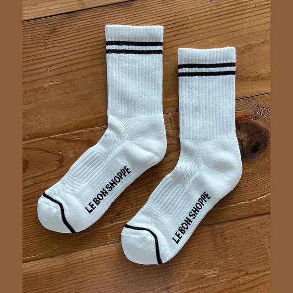 White socks with black stripes and 'Le Bon Shoppe' branding on a wooden surface