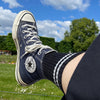 Navy Converse high-top sneaker with white laces worn on a grassy field with trees and blue sky.