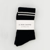 Black socks with white stripes and 'Le Bon Shoppe' label on a light gray background