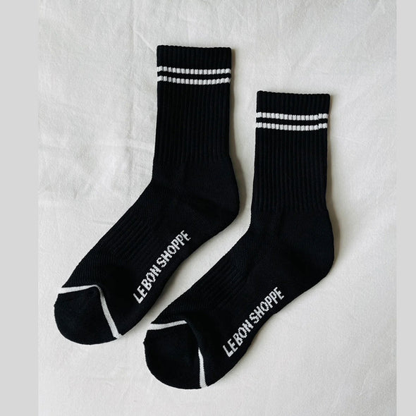 Black socks with white stripes and 'LE BON SHOPPE' branding on a light gray background
