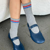 Person wearing gray socks with red and blue stripes and blue shoes on a concrete floor.