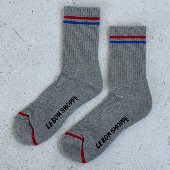 Gray socks with red and blue stripes and 'Le Bon Shoppe' branding on a light gray background