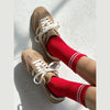 Beige sneakers with white laces worn with red socks on a light gray background