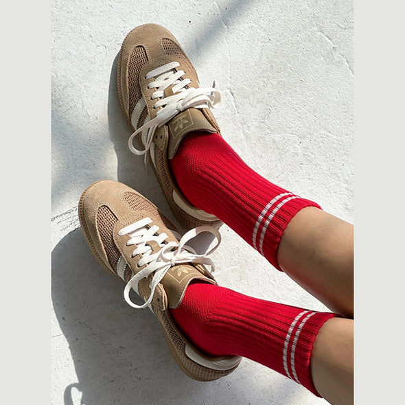Beige sneakers with white laces worn with red socks on a light gray background