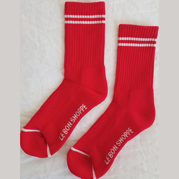 Red socks with white stripes and 'Le Bon Shoppe' branding on a light background