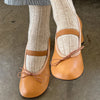 Brown leather shoes with bow detail worn with fawn socks on a concrete floor.