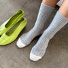 Grey socks with white toes and heels worn by a person, paired with green shoes on a neutral background.