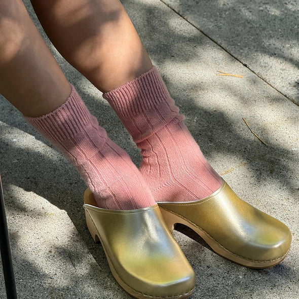 Person wearing pink socks and gold clogs on a concrete surface