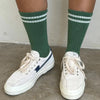White sneakers with a blue star logo worn with green socks on a concrete floor.