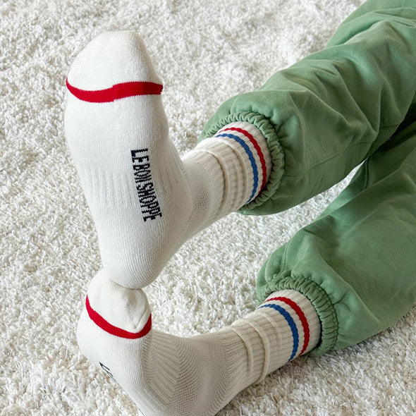 White socks with red and blue stripes and 'Le Bon Shoppe' branding on a light carpet.
