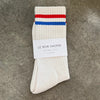 White sock with red and blue stripes on a gray surface, featuring 'Le Bon Shoppe' label.