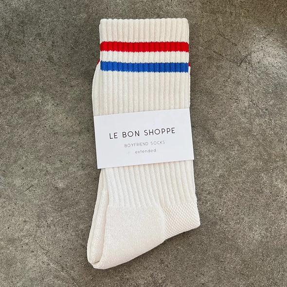 White sock with red and blue stripes on a gray surface, featuring 'Le Bon Shoppe' label.
