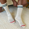 White socks with green and red accents worn by a person on a carpeted floor.
