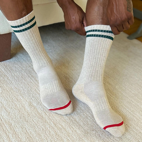 White socks with green and red accents worn by a person on a carpeted floor.