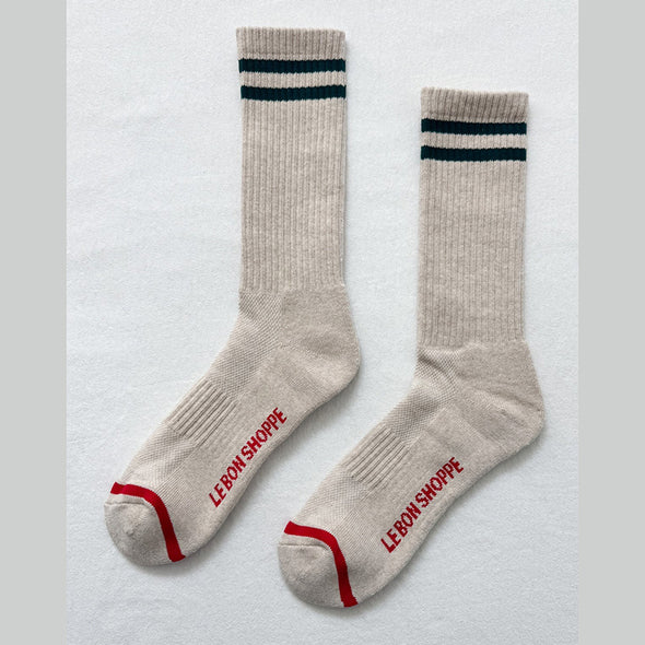 Pair of beige socks with black stripes and red accents on a light gray background