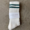 White sock with green stripes and 'Le Bon Shoppe' label on a textured surface