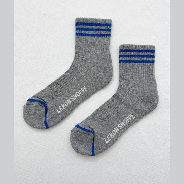 Grey socks with blue stripes and 'Le Bon Shoppe' branding on a light gray background