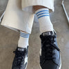 Person wearing black sneakers with 'GGDB' branding and white socks with blue stripes on a concrete floor.