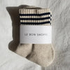 Beige sock with black stripes and 'Le Bon Shoppe' label on a gray background