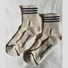 Pair of beige socks with black stripes and 'LEBON SHOPPE' branding on a light gray background