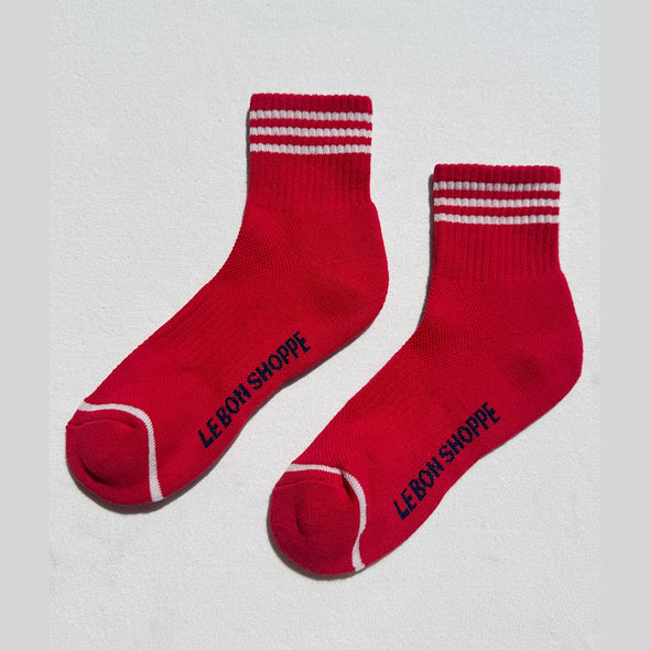 Red socks with white stripes and 'LE BON SHOPPE' branding on a light gray background