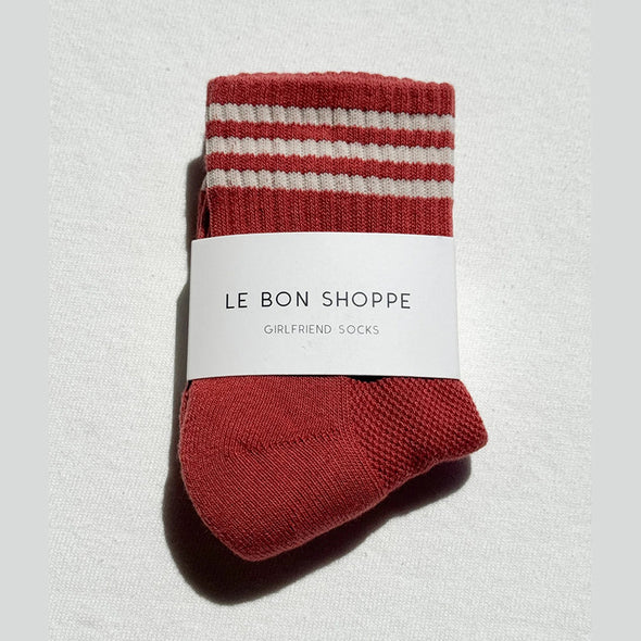 Terracotta sock with white stripes and 'Le Bon Shoppe' label on a light gray background