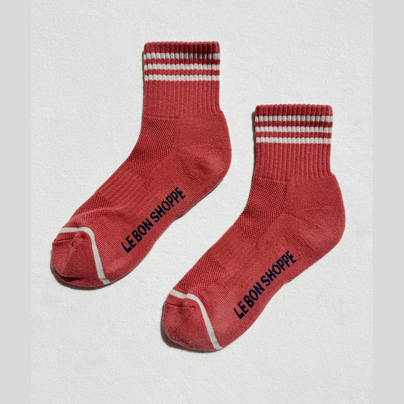Terracotta socks with white stripes and 'Le Bon Shoppe' branding on a light gray background